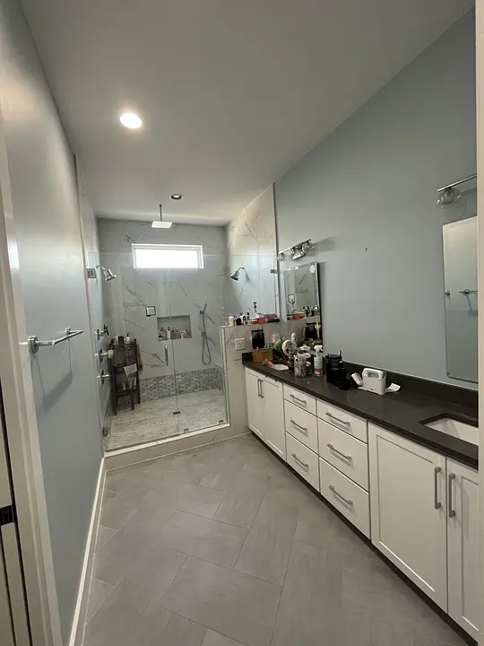 Modern bathroom with glass shower, white cabinets, and gray countertop. Blue walls and tiled floor.