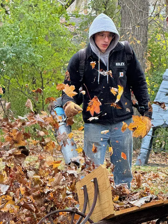 Team member using a leaf blower in a garden during autumn cleanup.