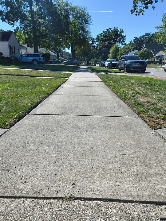 A sunny suburban street view with a concrete sidewalk and green lawns.