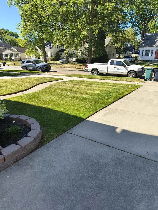 Sunny neighborhood street with green lawns and a KILEY white truck parked along the sidewalk.