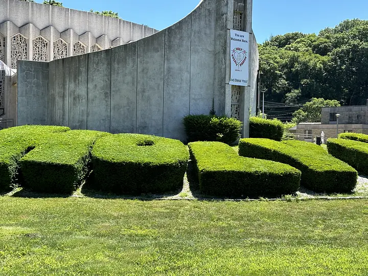 Hedge shaped into the word "HOLY" in front of a concrete church building with a banner.
