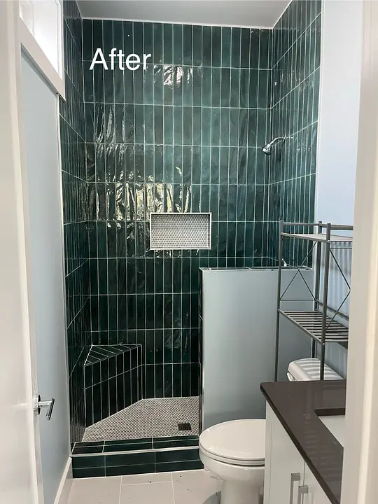 Renovated bathroom with dark green tiles, shower, and shelving.